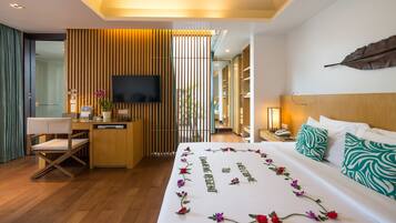 Una habitación de hotel moderna con un escritorio de madera, un televisor de pantalla plana, una cama con detalles florales y un ventanal grande.