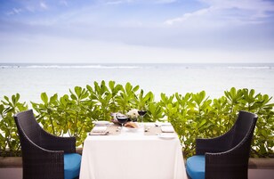 A table set for two with a view of the ocean, surrounded by lush green foliage.