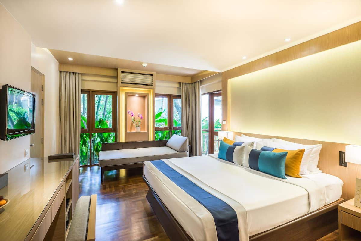 Habitación de hotel moderna con una cama grande, televisión, escritorio y vistas a zonas verdes por las ventanas.