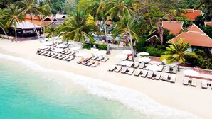 Un complexe hôtelier de bord de mer avec des chaises longues, des palmiers et des cabanes de plage.