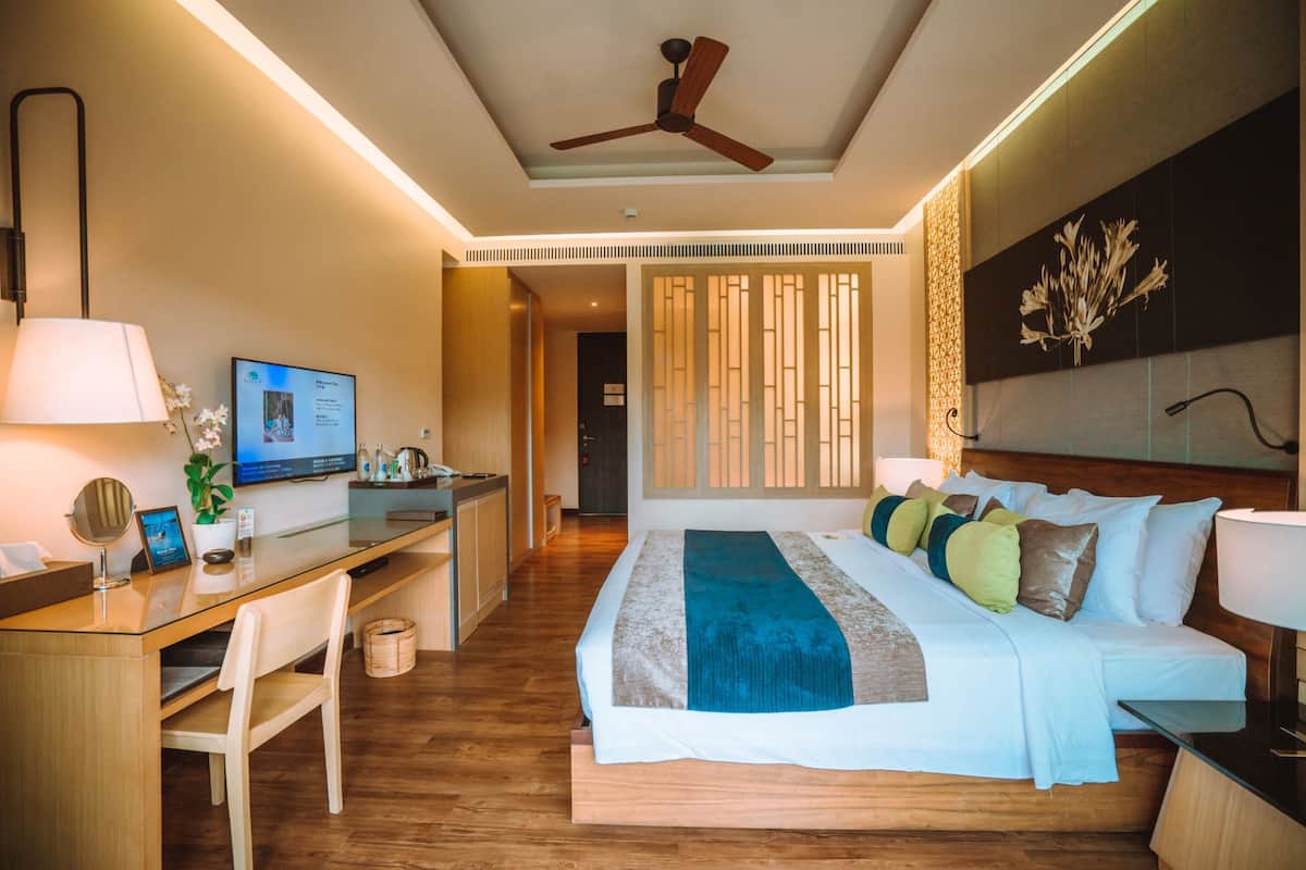 Una habitación de hotel con cama, escritorio, silla y ventilador de techo.