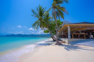 A beach with a building that has a covered area and palm trees.
