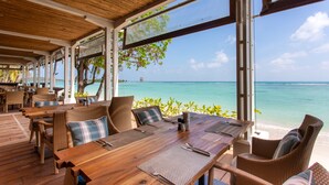 An outdoor seating area with wooden tables and wicker chairs, overlooking a beach and the ocean. - Chaweng Regent Beach Resort (Koh Samui)