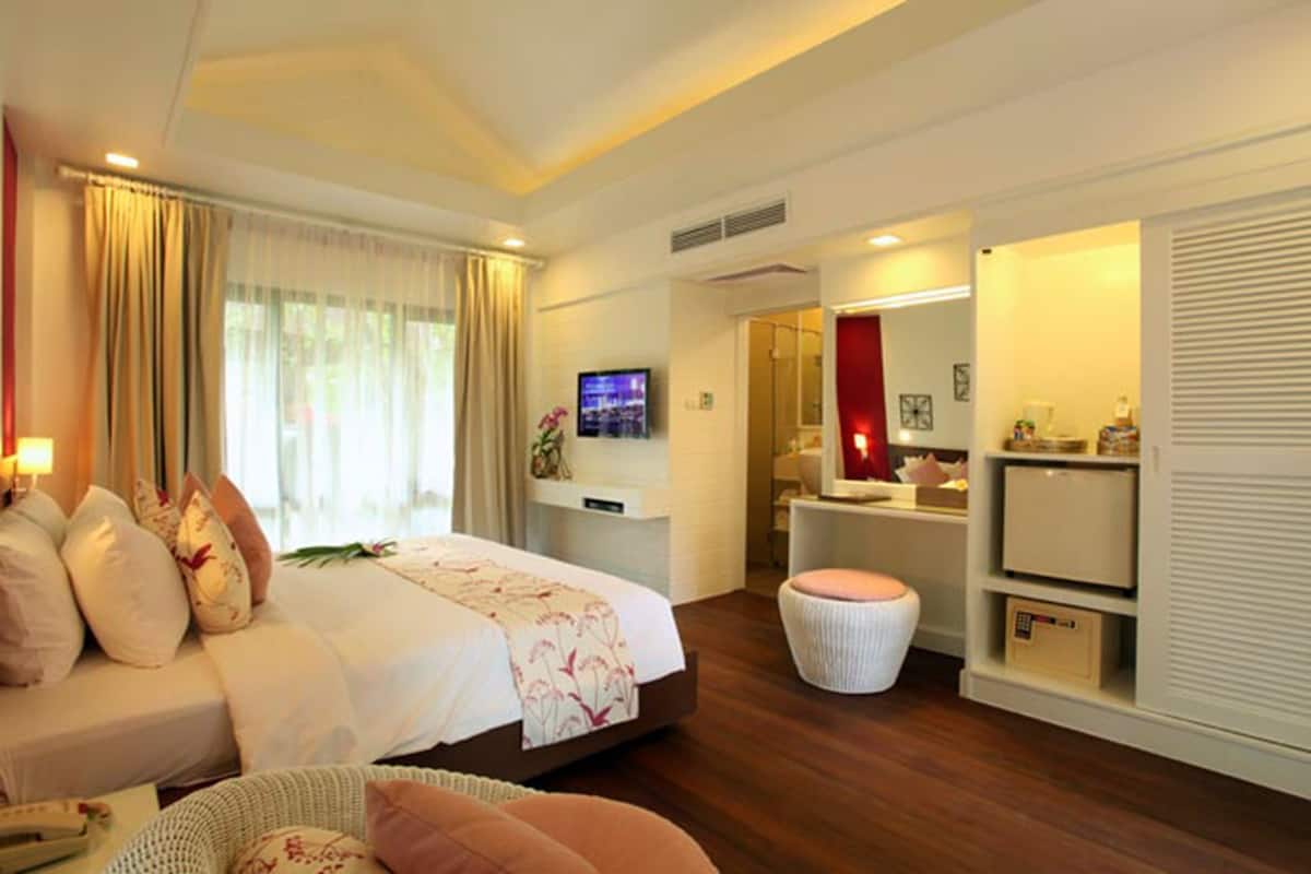 Habitación de hotel moderna con una cama grande, televisor, tocador con espejo y un pequeño rincón de descanso.
