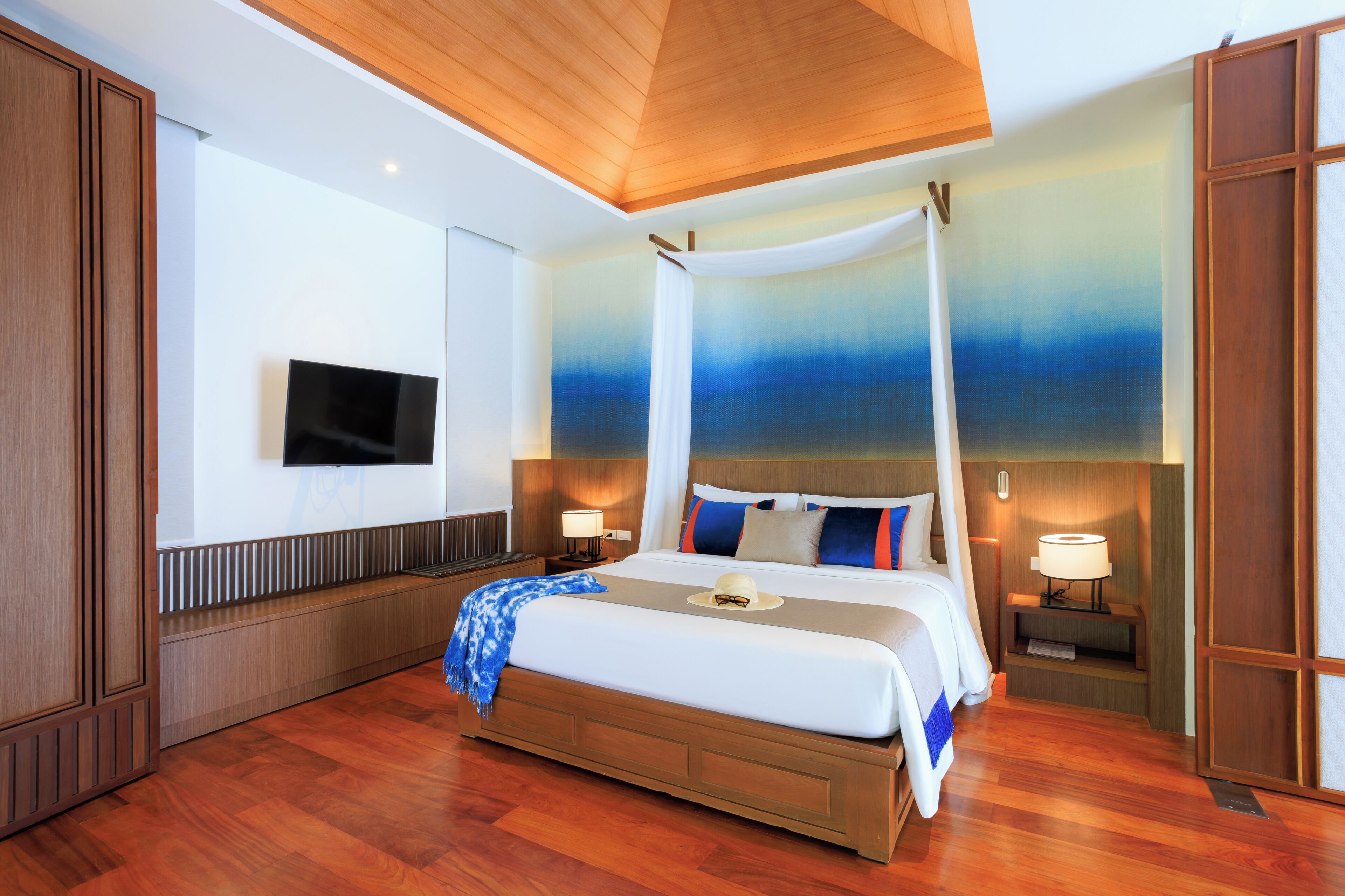 Amplia habitación de hotel con una cama grande, piso de madera, televisor montado en la pared y un techo con diseño de madera.