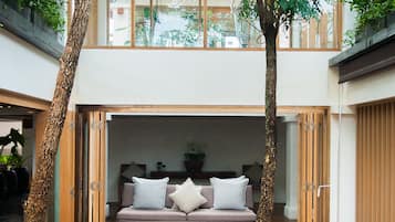 A modern interior with a wooden deck, a sofa with cushions, and a large tree in the center.