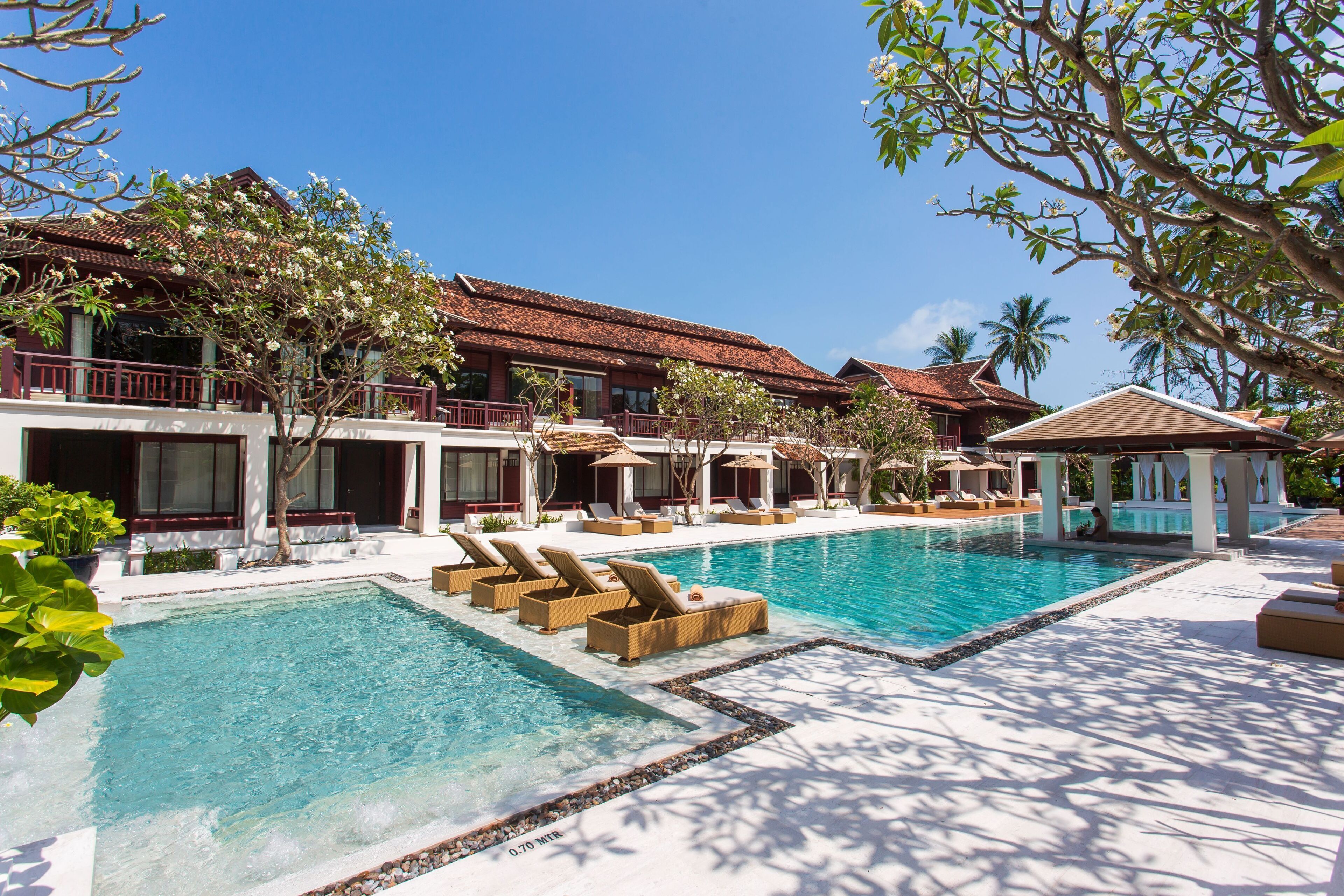 A resort with a large pool, lounge chairs, and a building with a red roof.