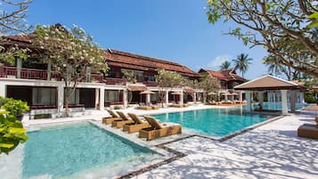A resort with a large pool, lounge chairs, and a building with a red roof.