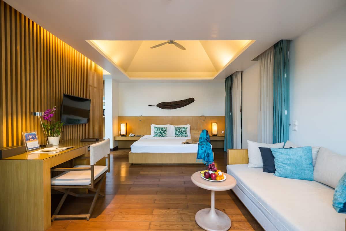 Una habitación de hotel moderna con una cama, un escritorio, un sofá y una pequeña mesa con fruta.