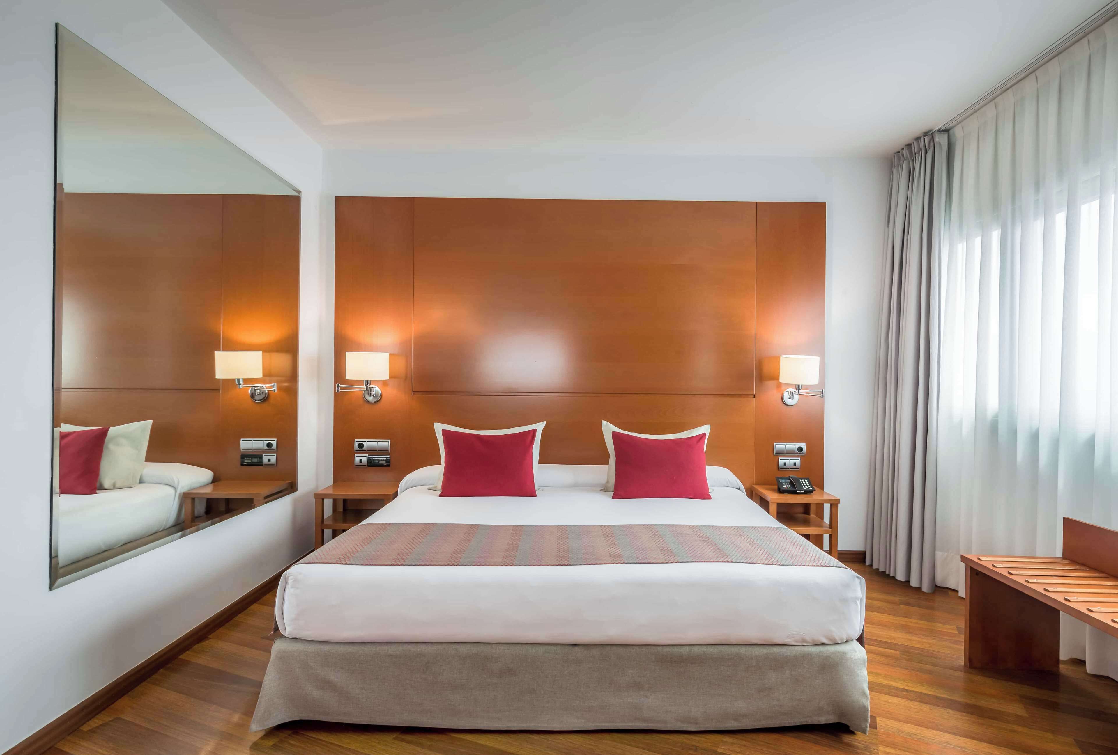 A hotel room with a large bed, two bedside tables, a mirror, and a window with curtains.