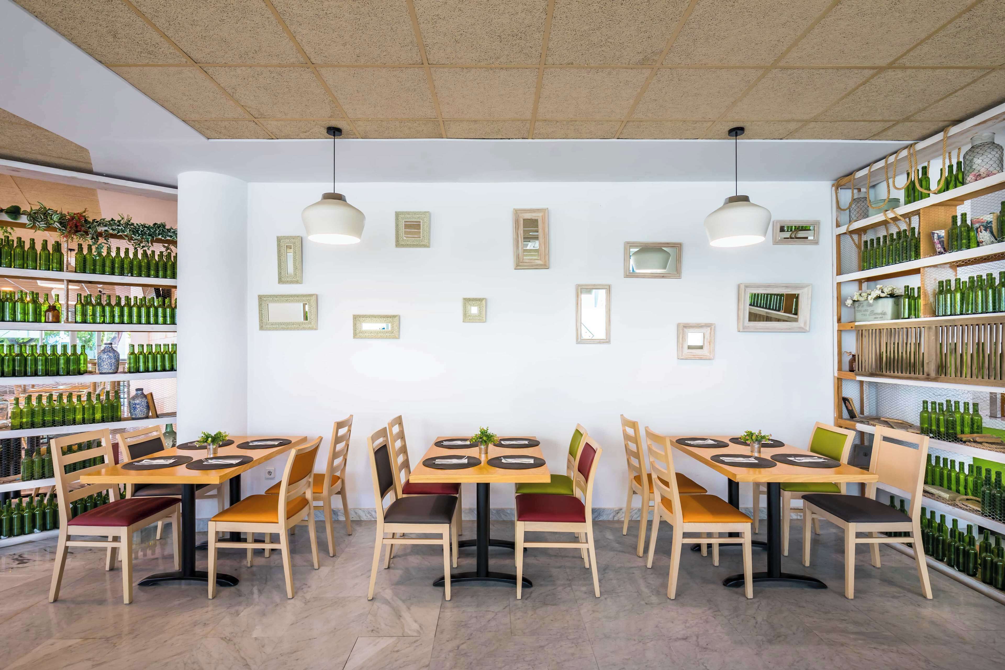 A restaurant interior with multiple tables and chairs, shelves with bottles, and framed pictures on the walls.