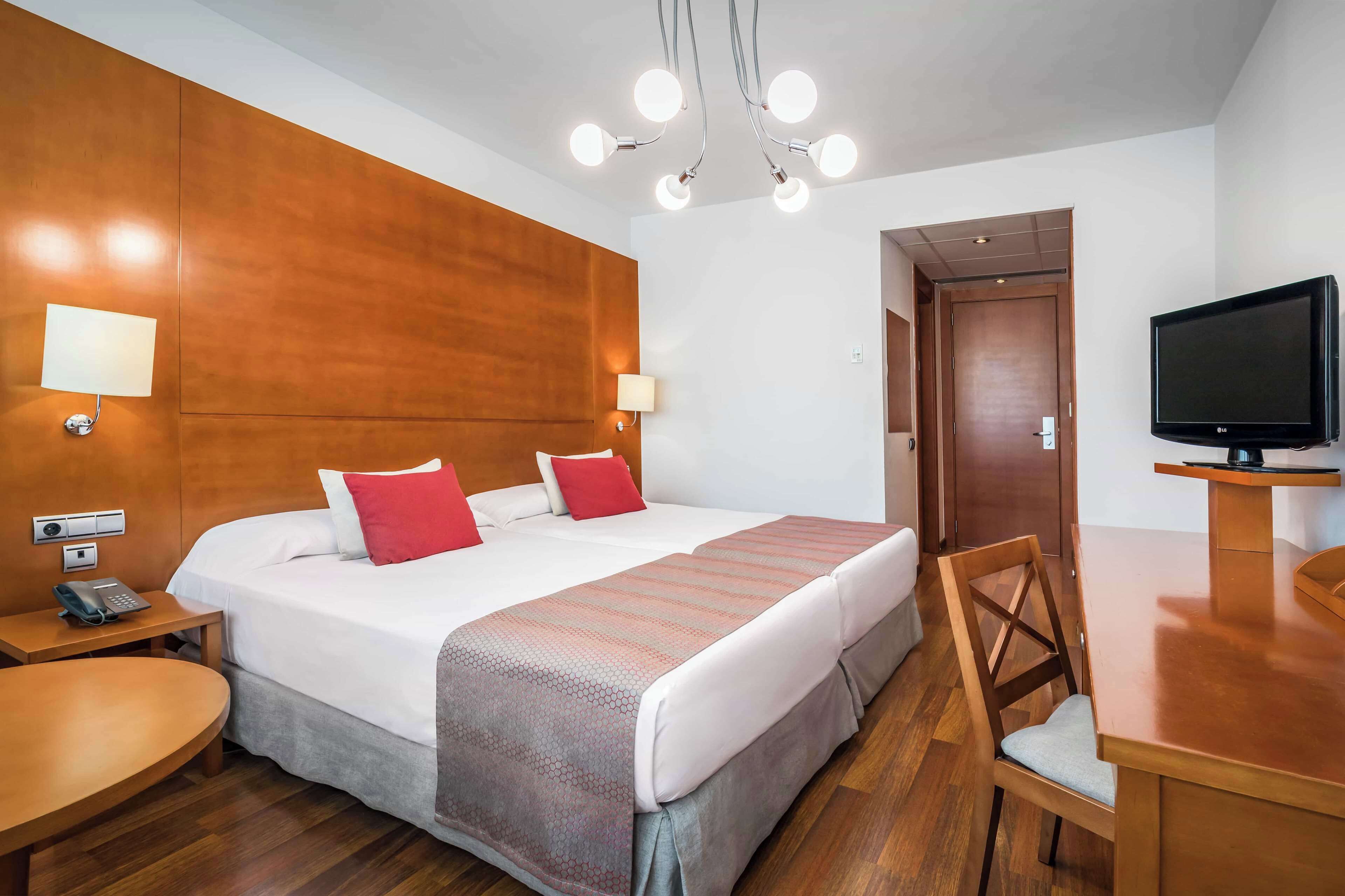 Habitación de hotel con una cama grande, cabecera de madera, escritorio con silla, televisor y teléfono en la mesita de noche.
