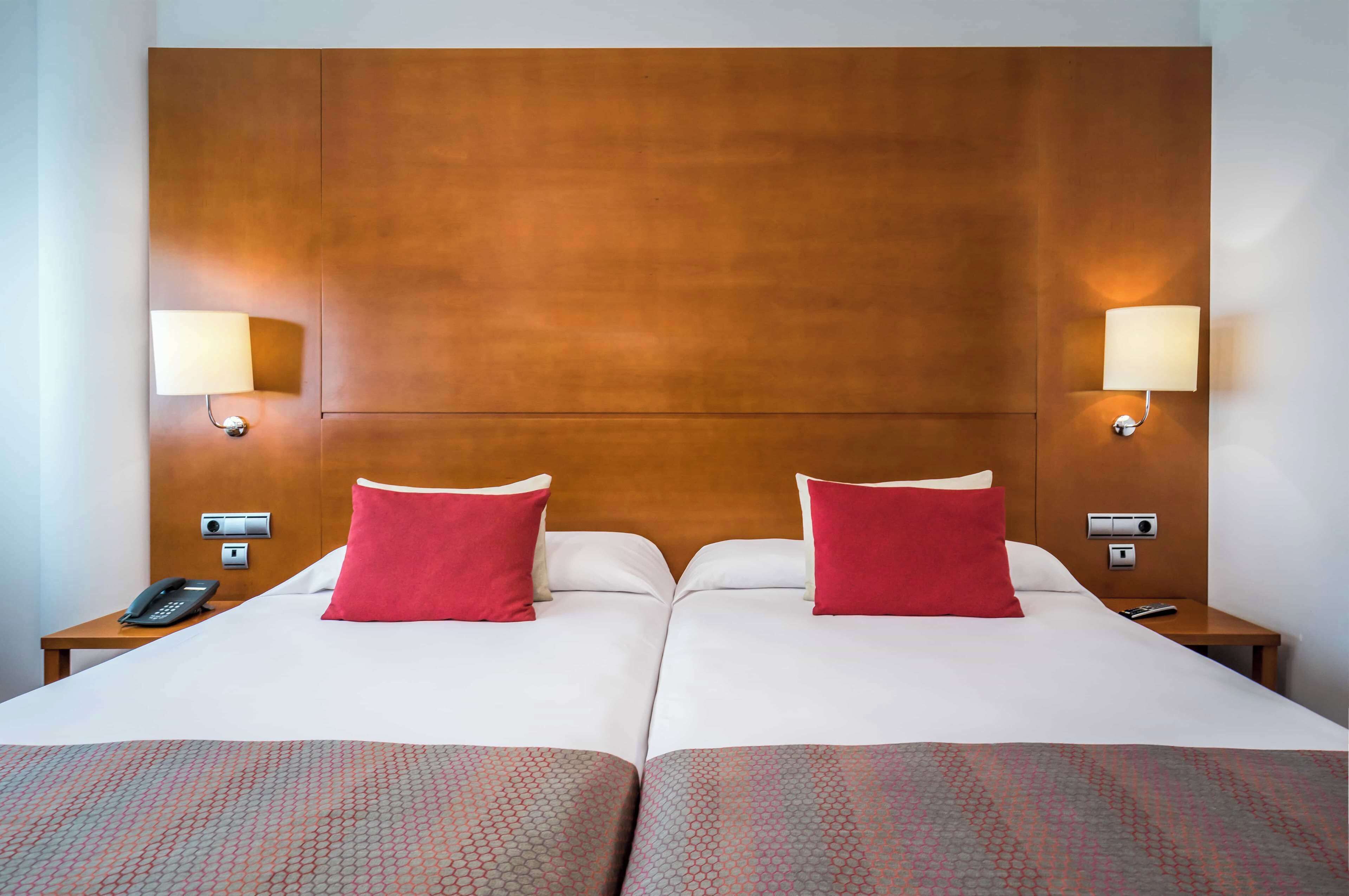 Habitación de hotel con una cama grande, dos mesitas de noche, un teléfono y lámparas de pared.