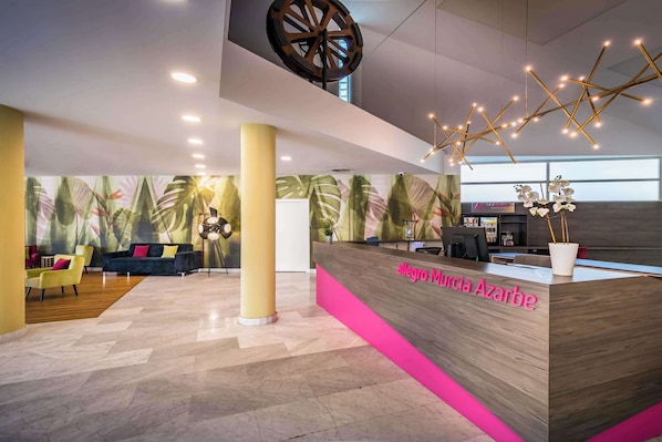 A hotel reception area with a modern design, featuring a reception desk, seating area, and a large window providing natural light.