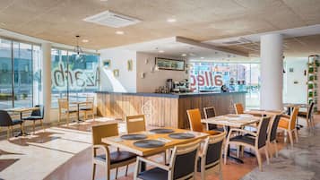 Un café moderno con mesas y sillas, una barra con menú y ventanas amplias.