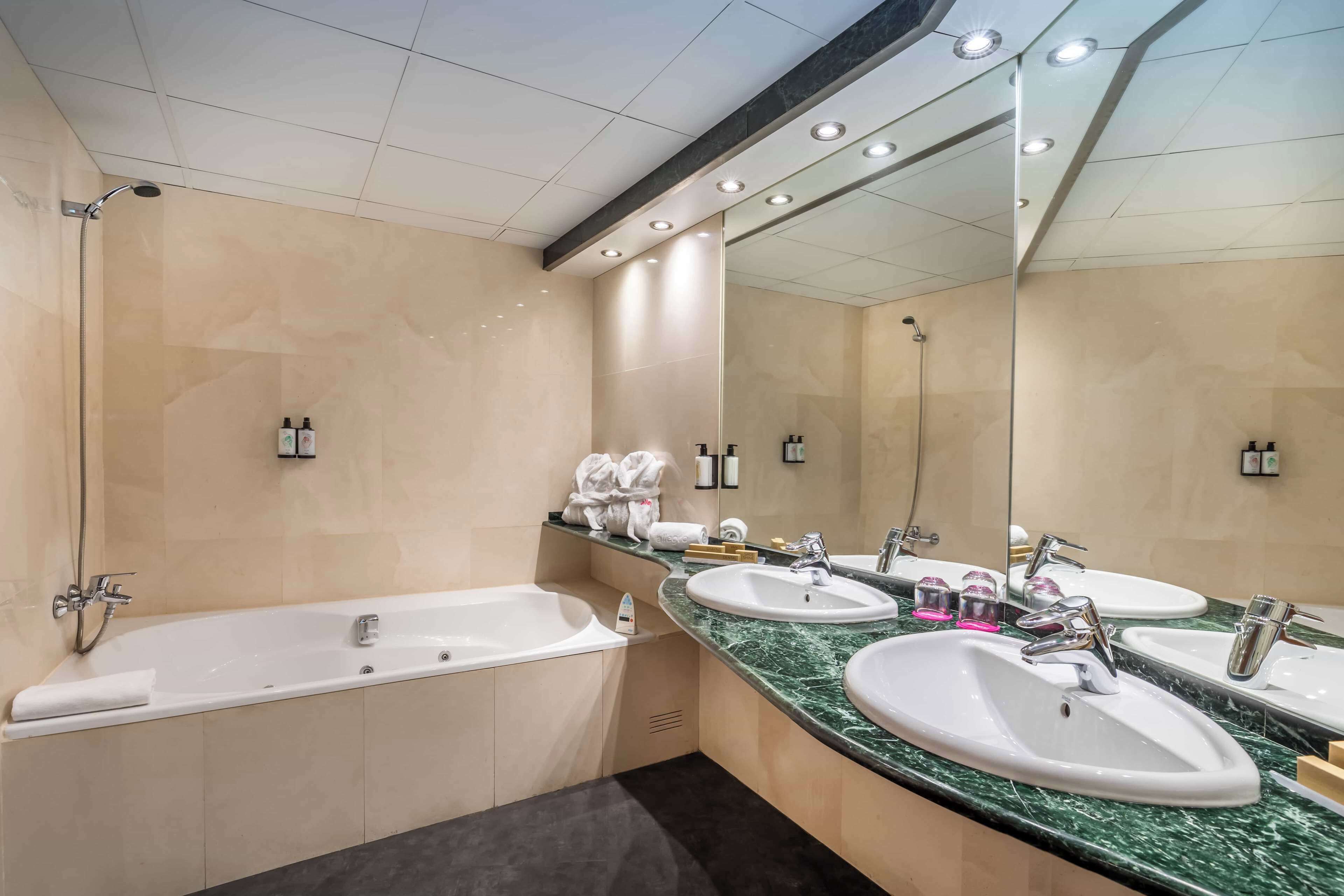 Un baño moderno con bañera, dos lavamanos y un espejo grande.