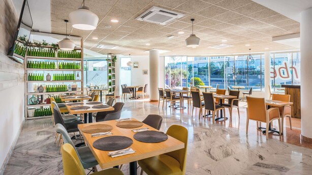 Un restaurant spacieux avec de hauts plafonds, un éclairage moderne à suspension et différents types d’aménagements pour les places assises.