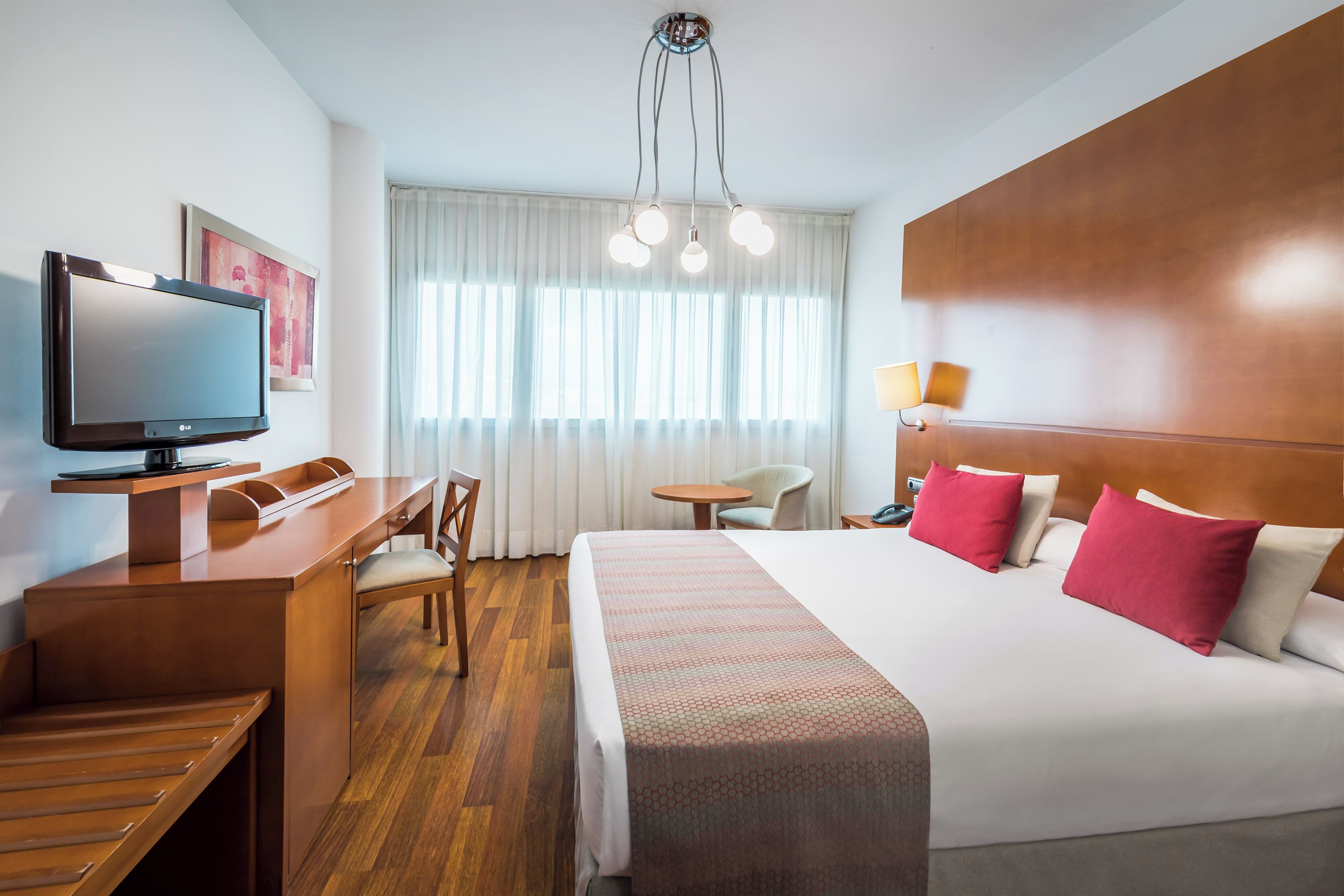 A hotel room with a bed, desk, chair, television, and a window with curtains.