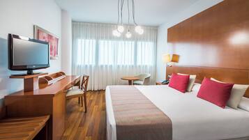 Una habitación de hotel con cama, escritorio, silla, televisor y ventana con cortinas.