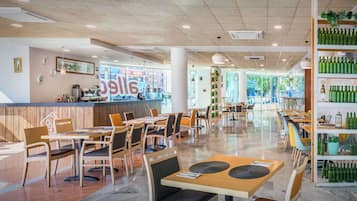 Un restaurante espacioso con mesas y sillas de madera, una zona de bar y un estante con botellas verdes.