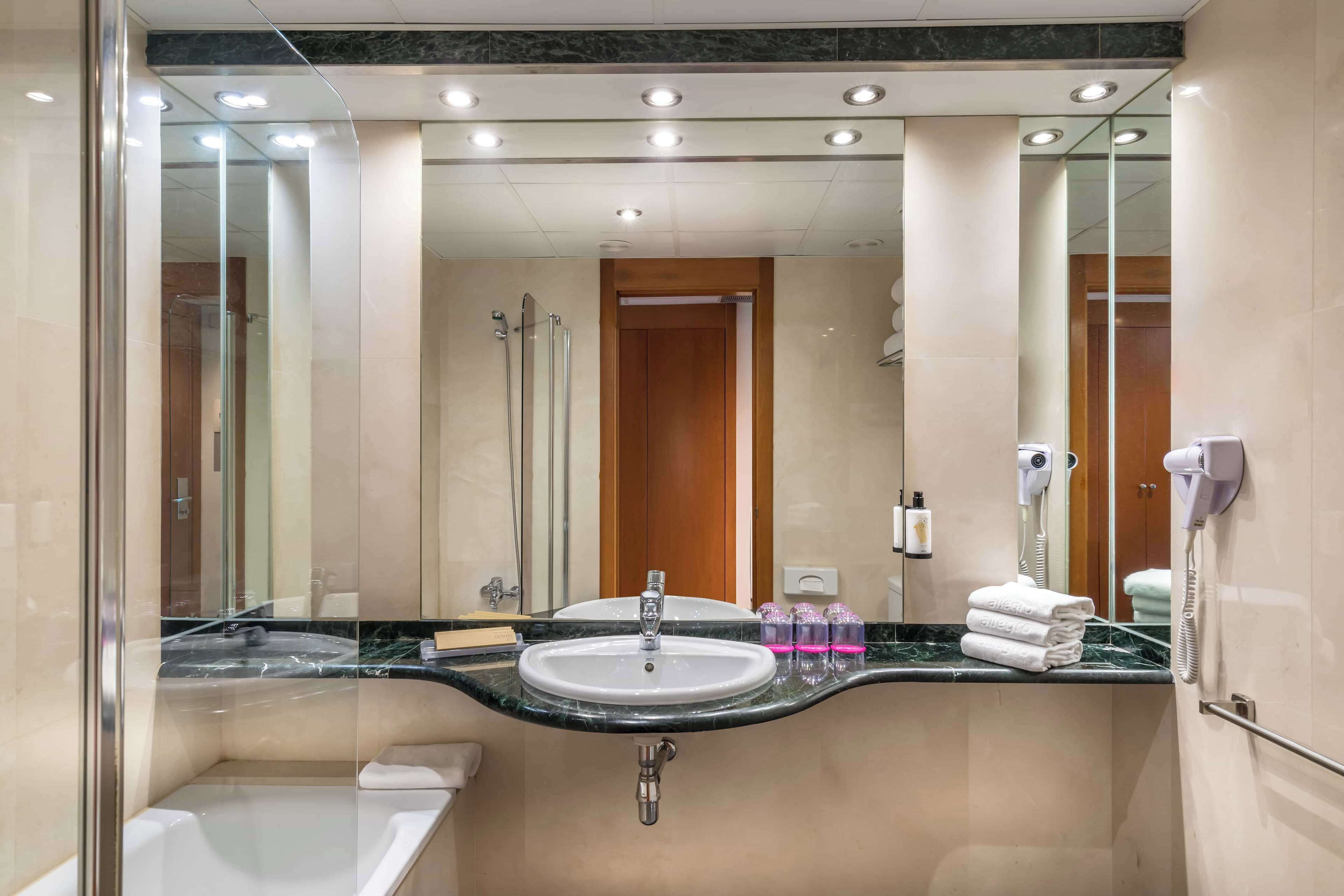 A modern bathroom with a large mirror, a sink, a shower, and a hairdryer.