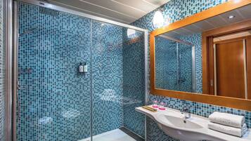 Un baño con cabina de ducha de vidrio, un lavabo blanco y un espejo con marco de madera.