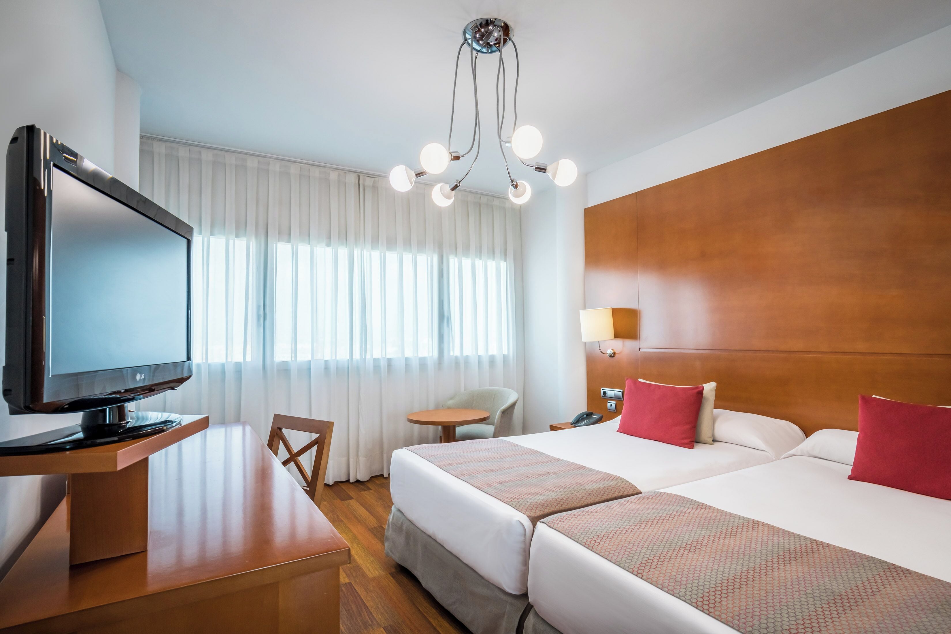 A hotel room with a TV, two beds, a desk, and a chair.