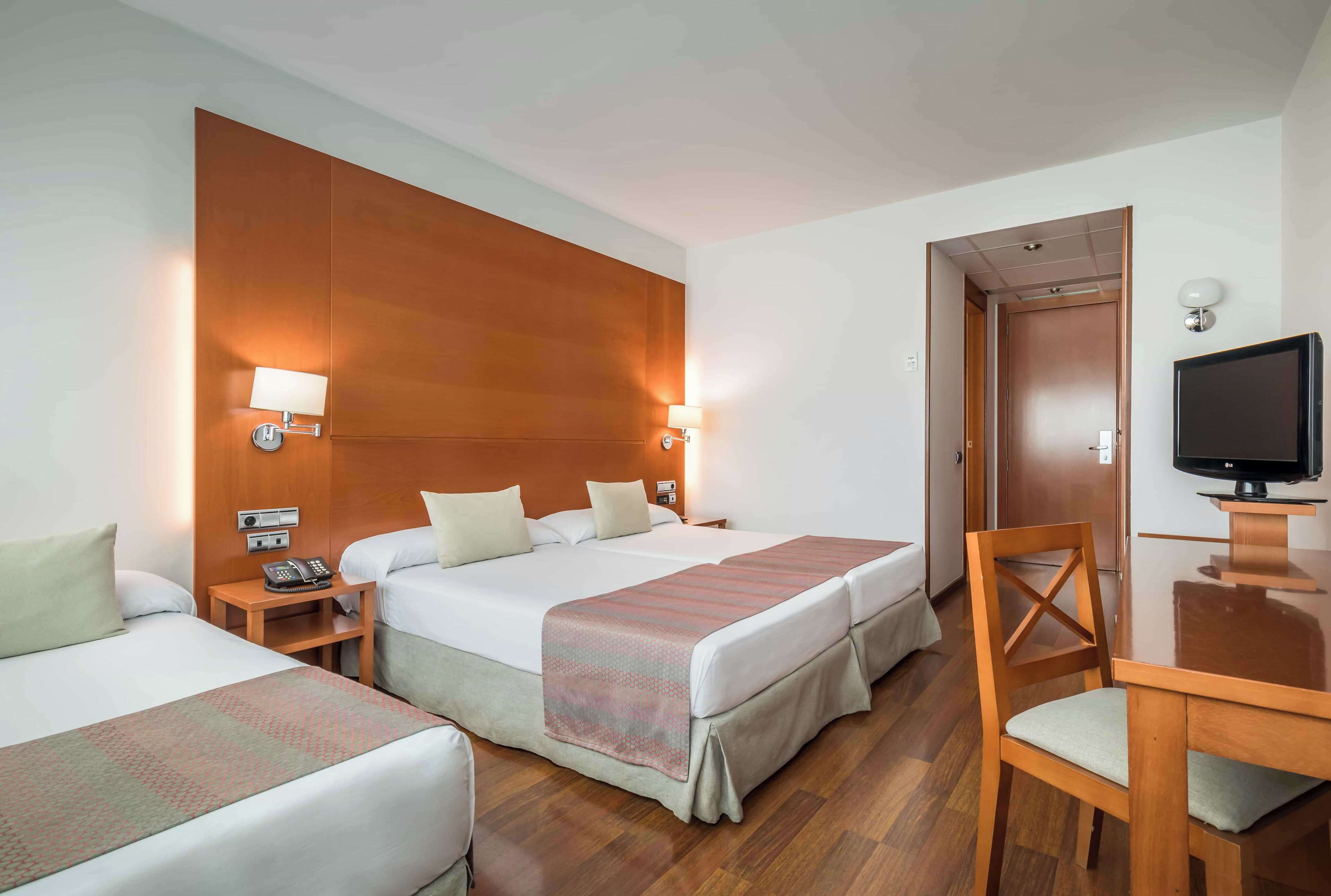 Een hotelkamer met twee bedden, een bureau, een televisie en een houten wandpaneel.