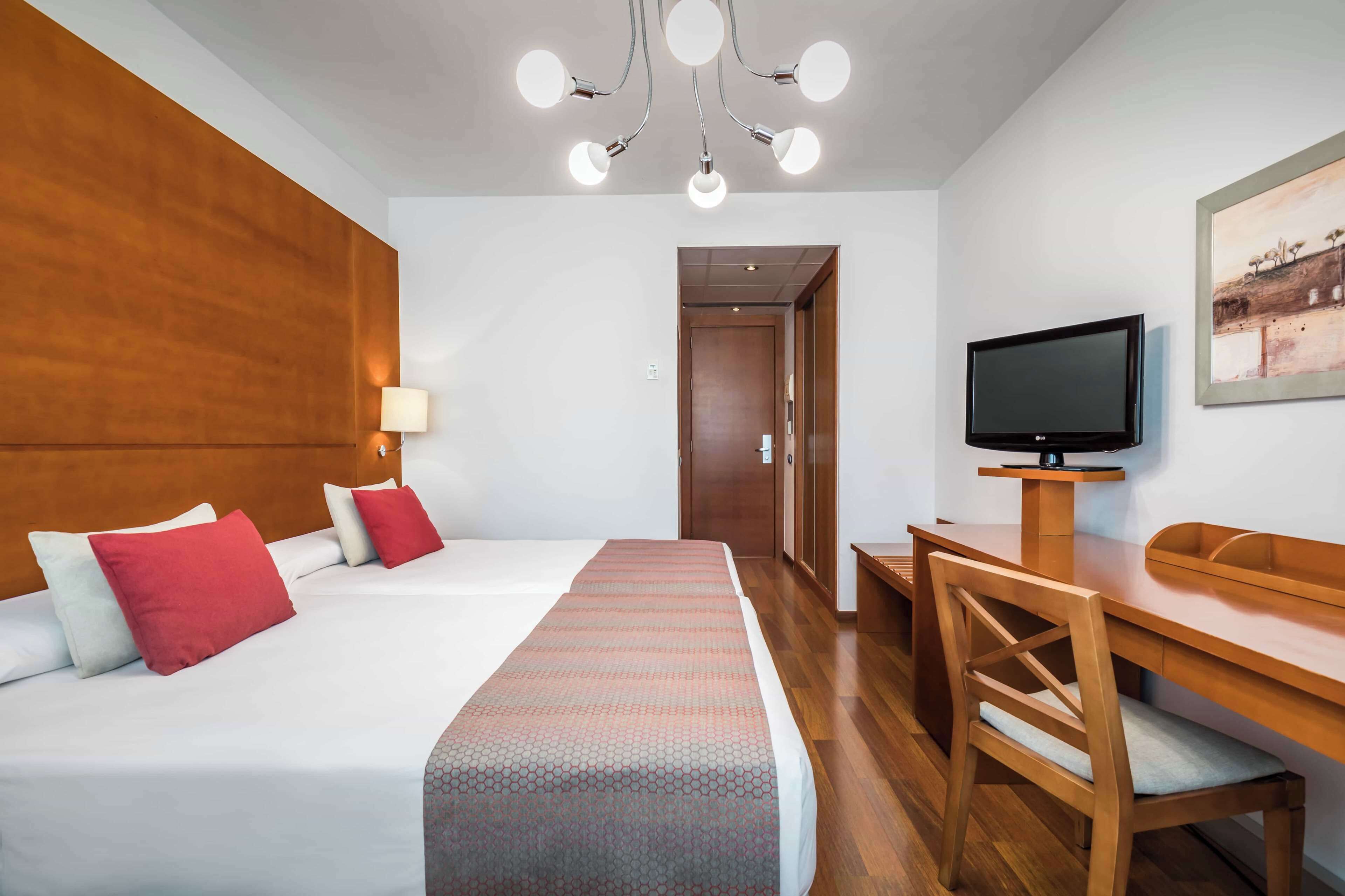 A hotel room with a bed, a desk, a chair, a television, and a painting on the wall.