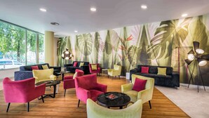 Un espace de détente moderne doté d’une grande fenêtre, d’une fresque représentant des feuilles tropicales et de différents types de sièges, notamment des canapés et des fauteuils.