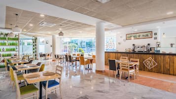 A modern restaurant with a clean, open layout, featuring a central bar area, multiple seating options, and a view of the outdoors through large windows.