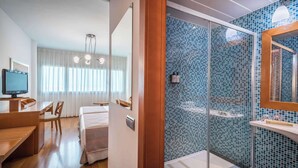 Une chambre d’hôtel avec un bureau en bois, un lit, une télévision et une salle de bain dotée d’une douche en verre et de carreaux de mosaïque bleus.