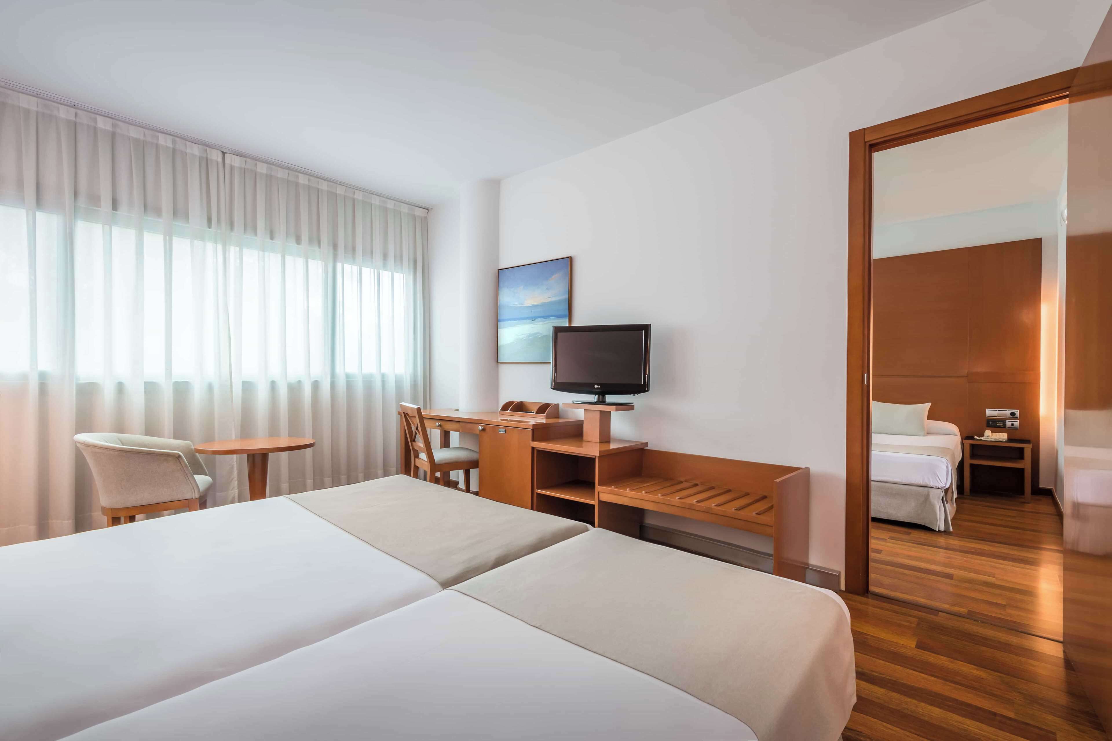 Una habitación de hotel con una cama grande, un escritorio con una silla, un televisor y un cuadro en la pared.