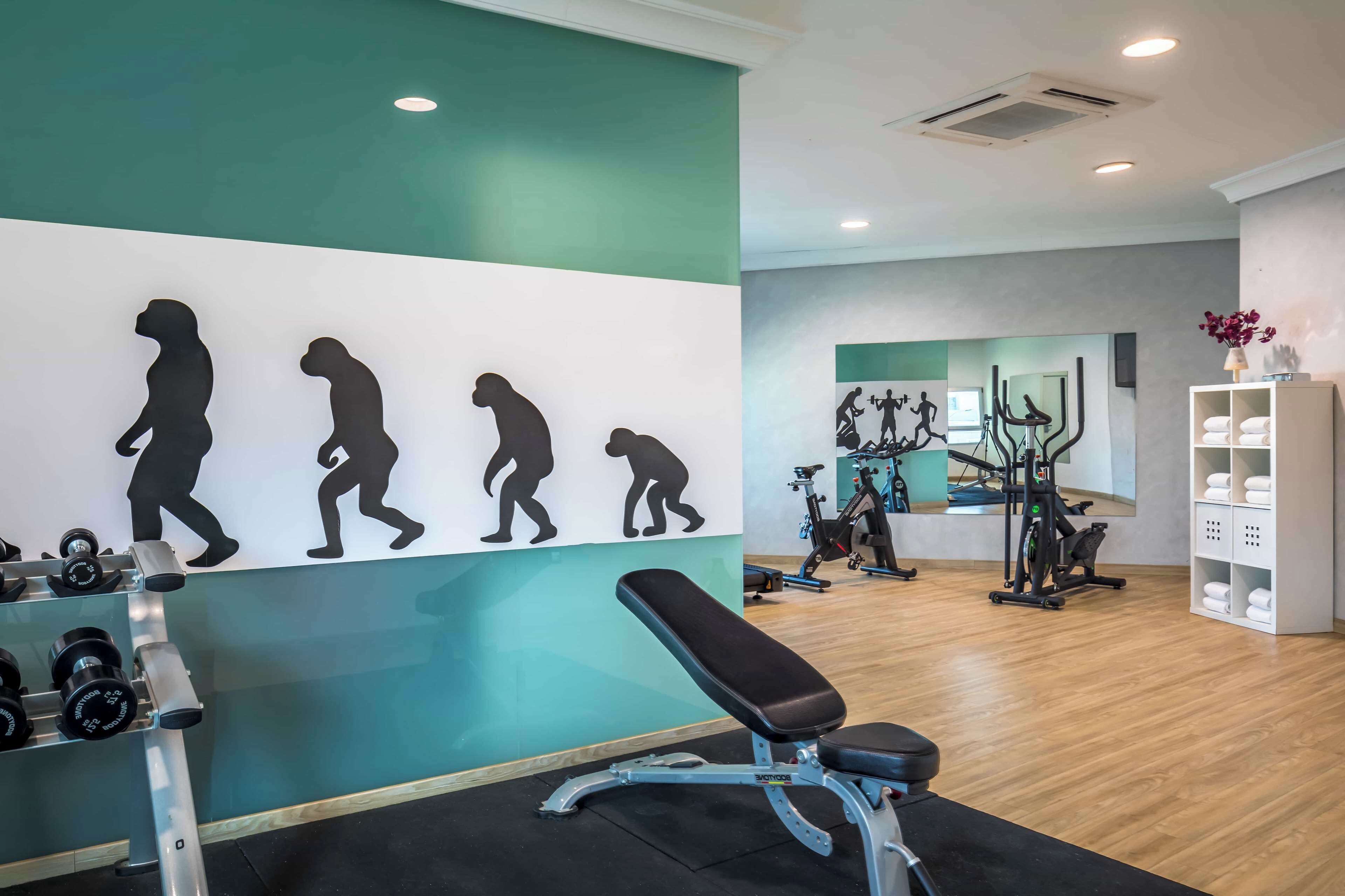 Un gimnasio con equipo de ejercicio, una pared con siluetas y un banco.