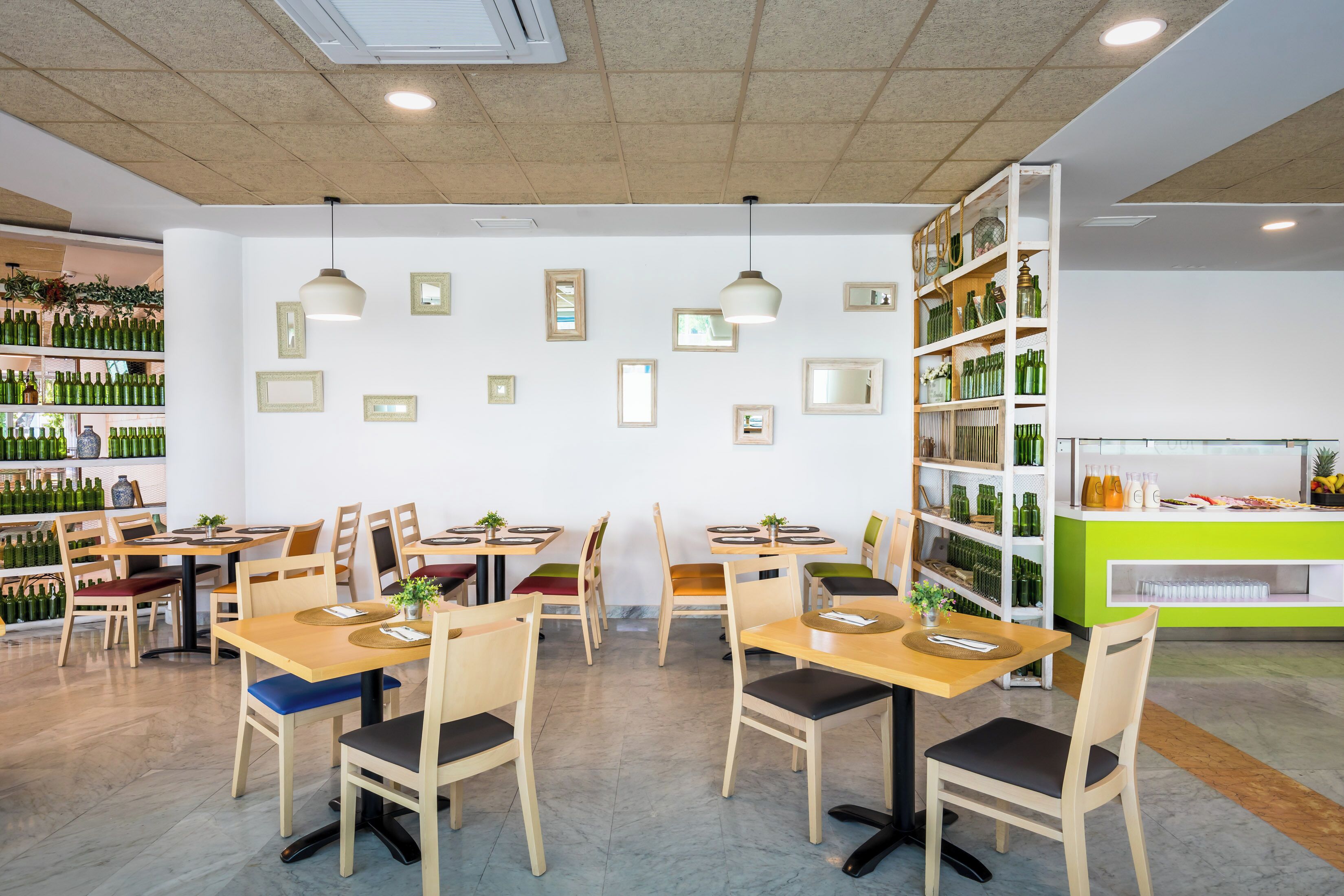 A restaurant with wooden tables and chairs, a green counter, and shelves with bottles and glasses.