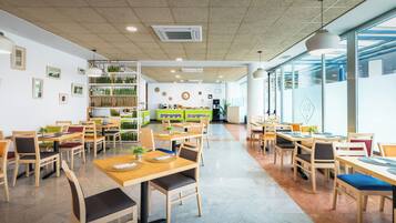 A spacious restaurant with wooden tables and chairs, a central counter, and a view through large windows.