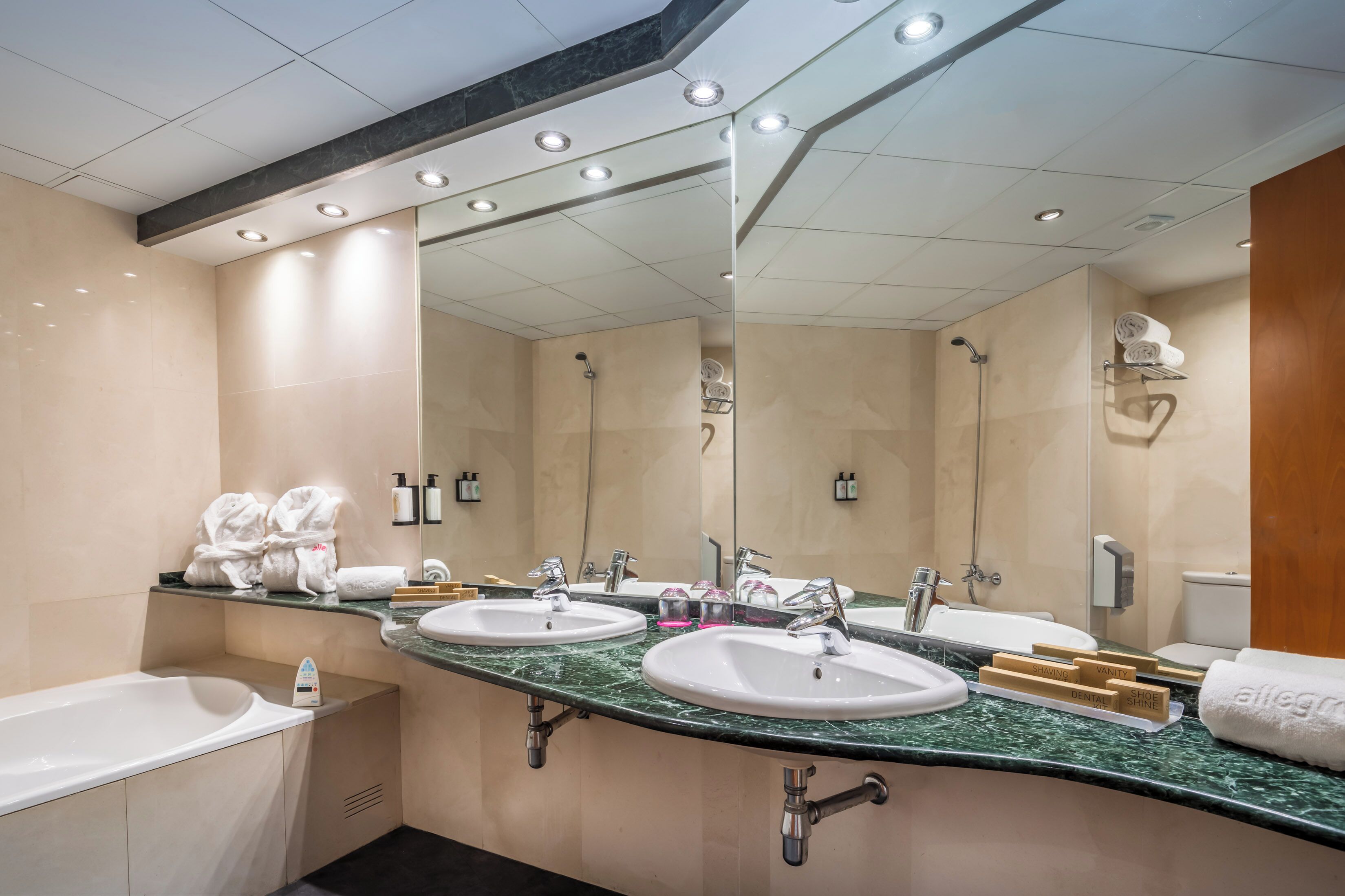 Een moderne badkamer met twee wasbakken, een bad en een grote spiegel.