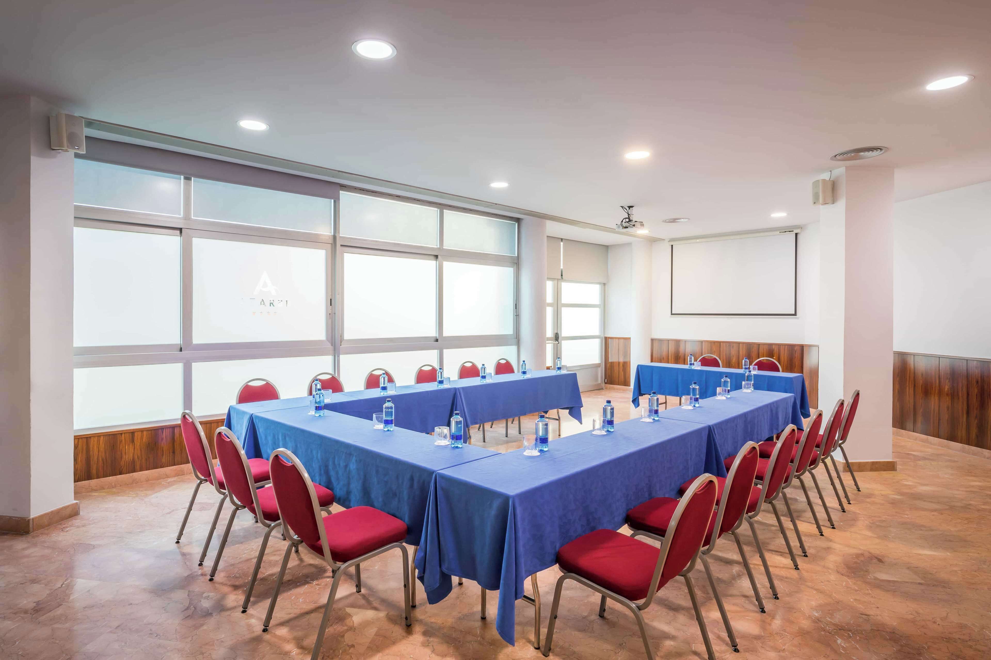 A conference room with long tables, red chairs, and large windows.