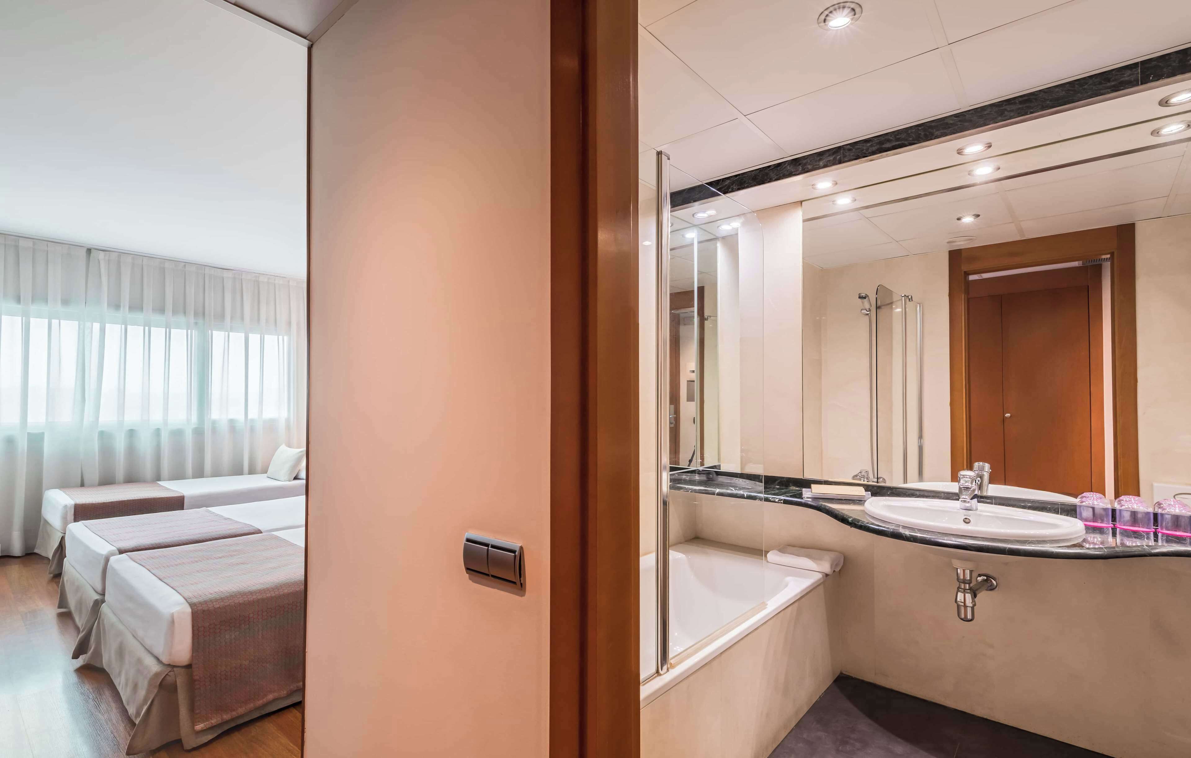 A hotel room with two beds, a large mirror, a sink, and a shower.