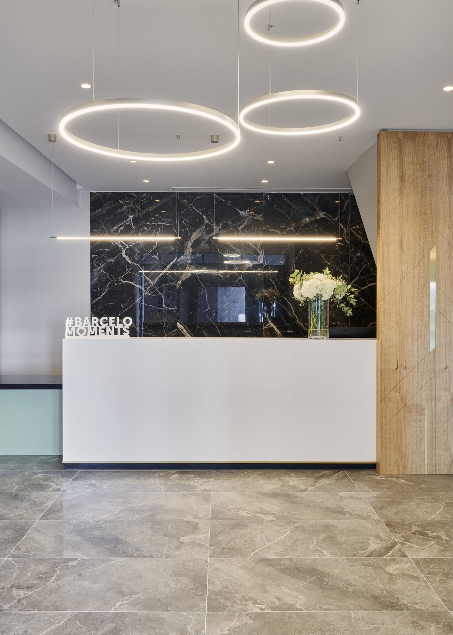 Un área de recepción moderna con una pared de mármol, un mostrador blanco y un panel de madera a la derecha.