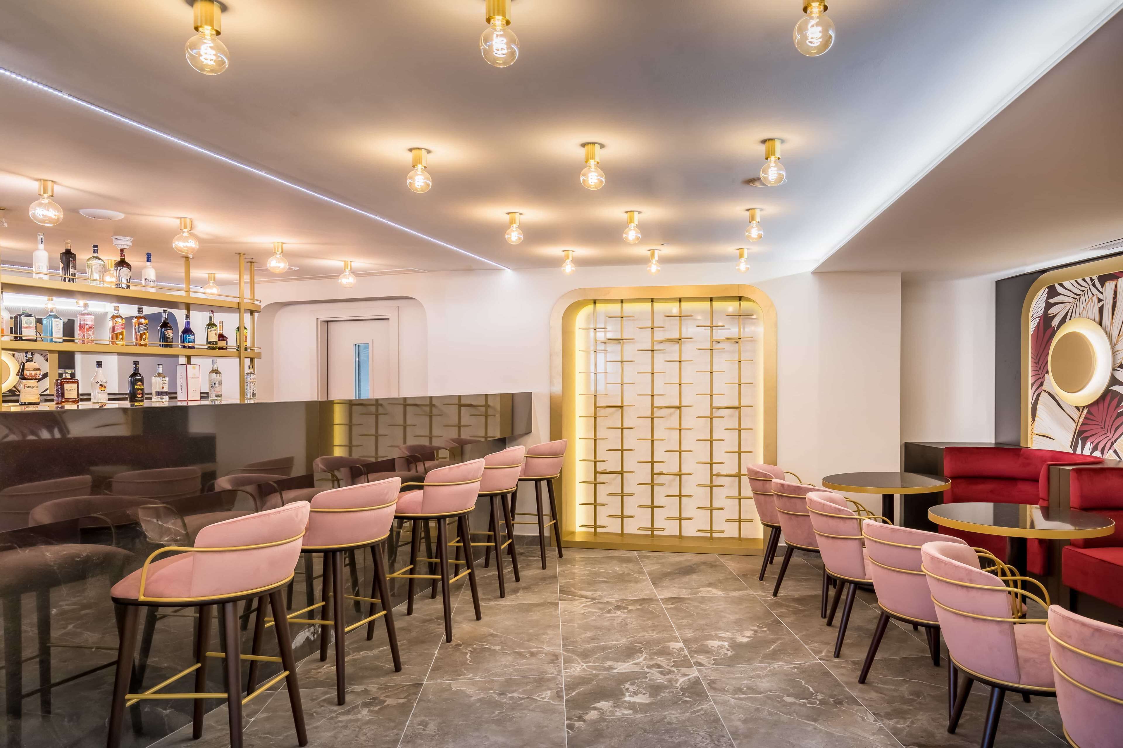 A modern bar area with bar stools, a counter with bottles, and a seating area with round tables and chairs.