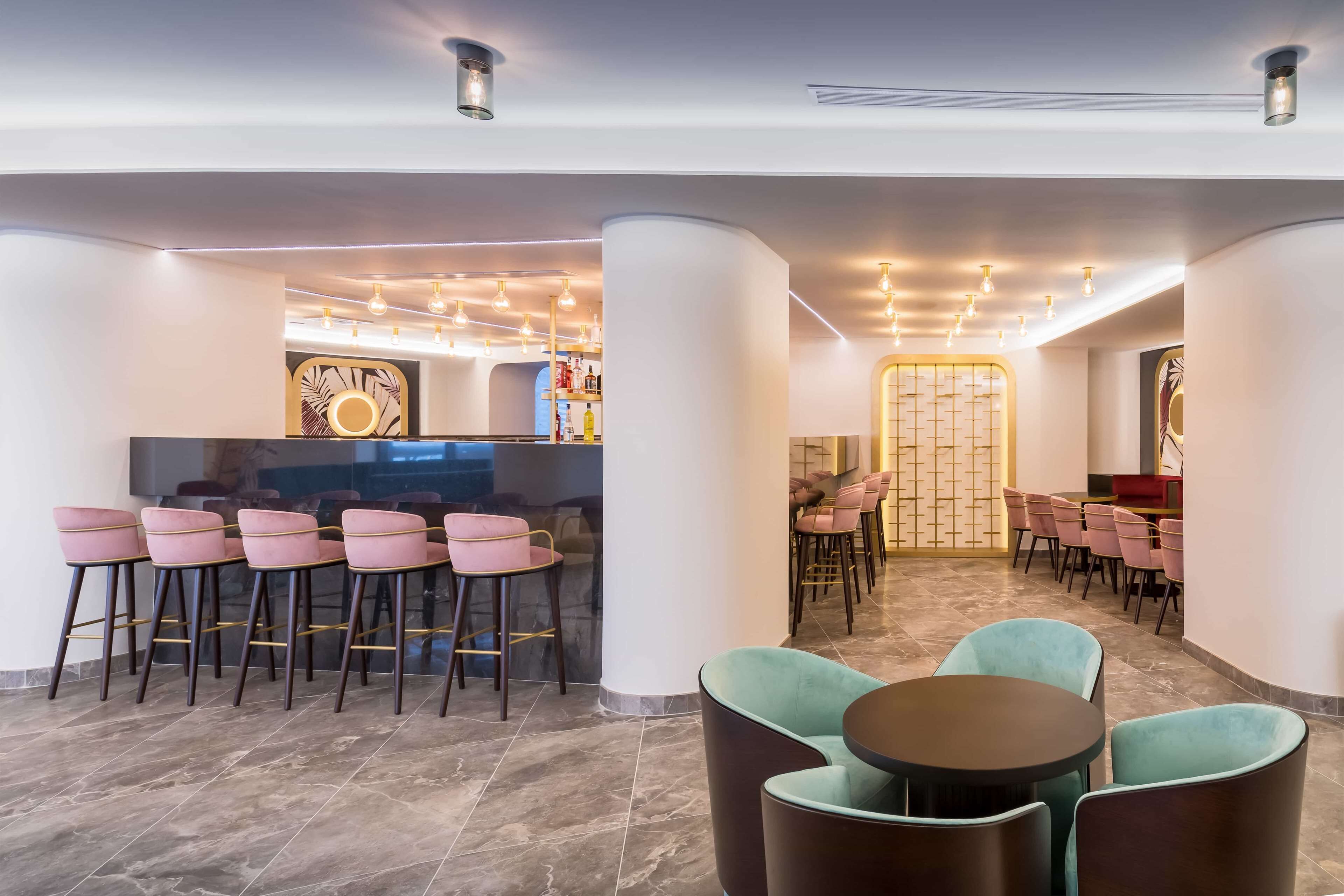Un'area bar moderna con sgabelli alti, un bancone e una zona con tavoli rotondi e sedie.