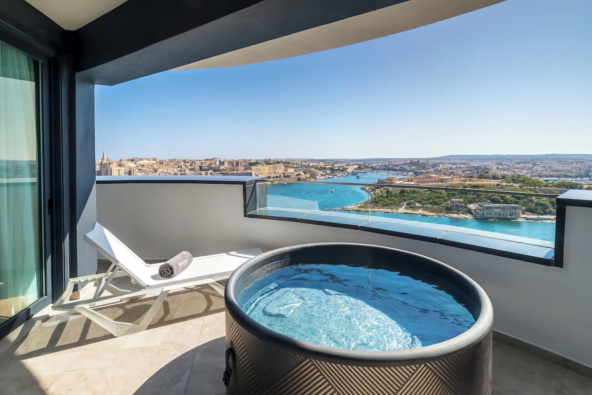 A balcony with a hot tub and a view of a coastal cityscape.