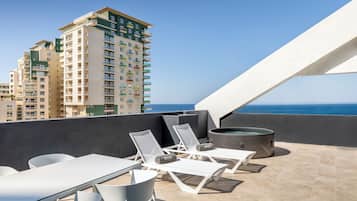 Terraço no telhado com cadeiras de lounge brancas, uma mesa e uma banheira de hidromassagem.