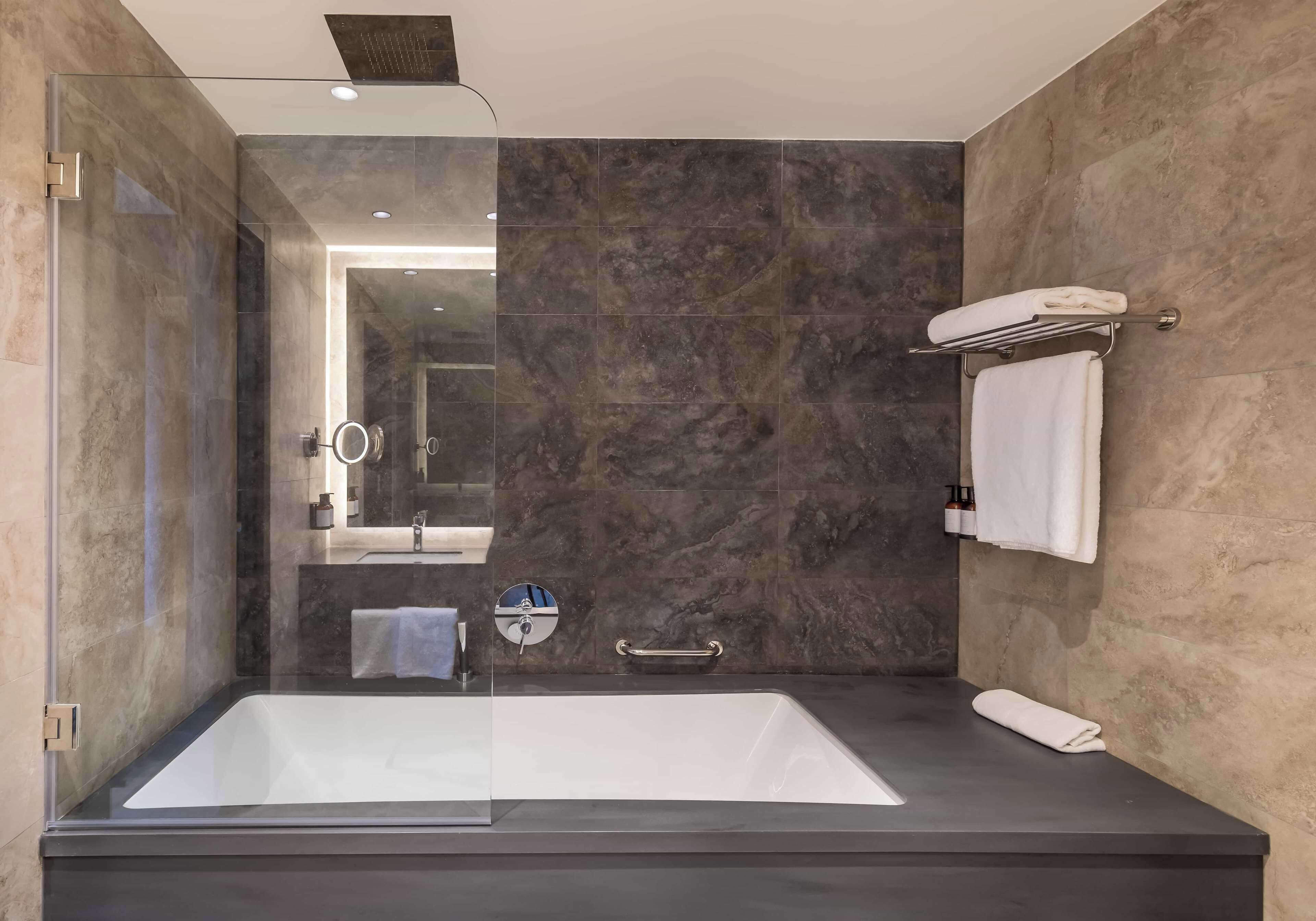 Ein modernes Badezimmer mit einer großen Badewanne, einer Glaskabine zur Dusche und Marmorwänden.