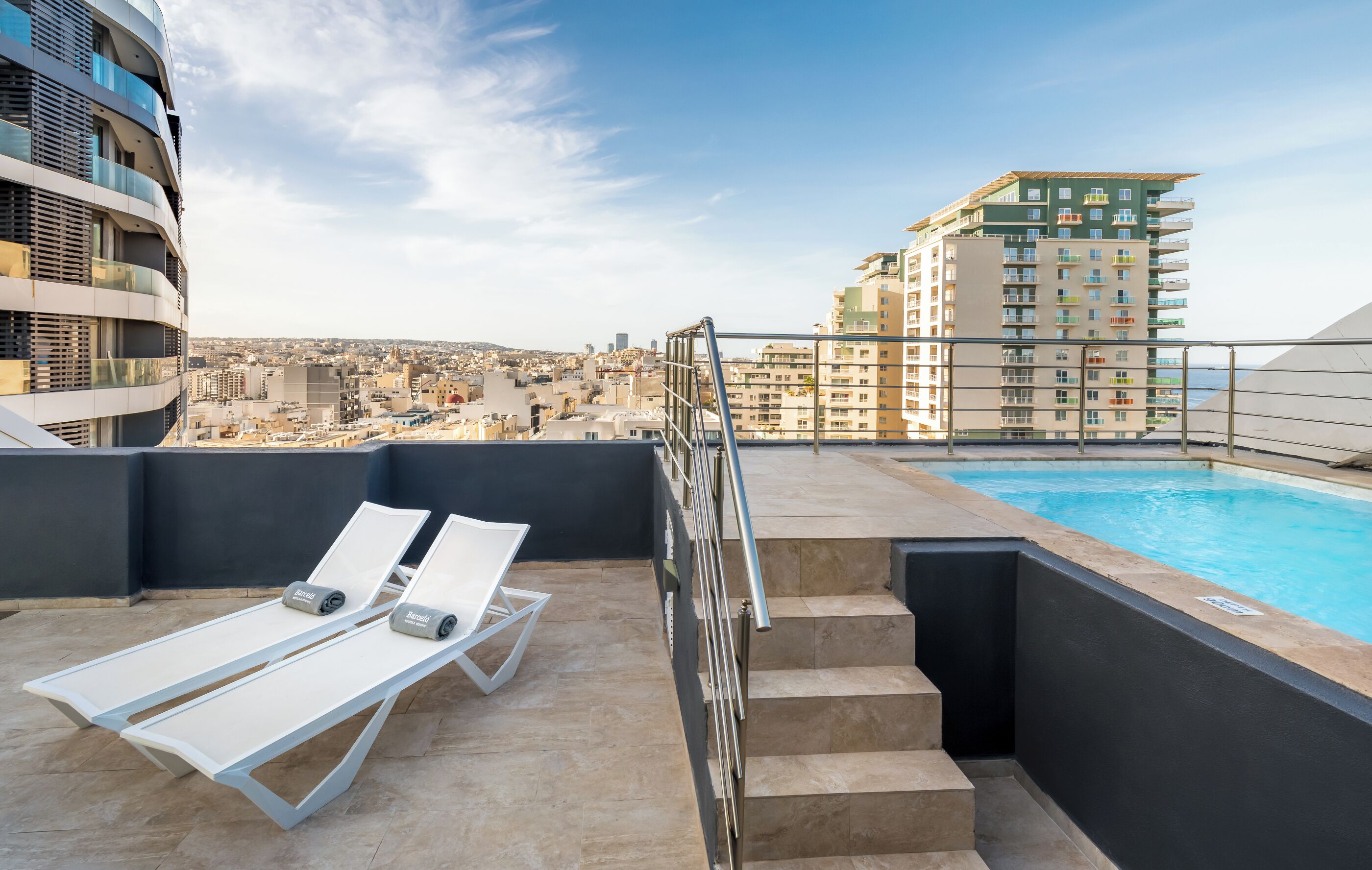 A rooftop pool area with lounge chairs and a view of the cityscape.