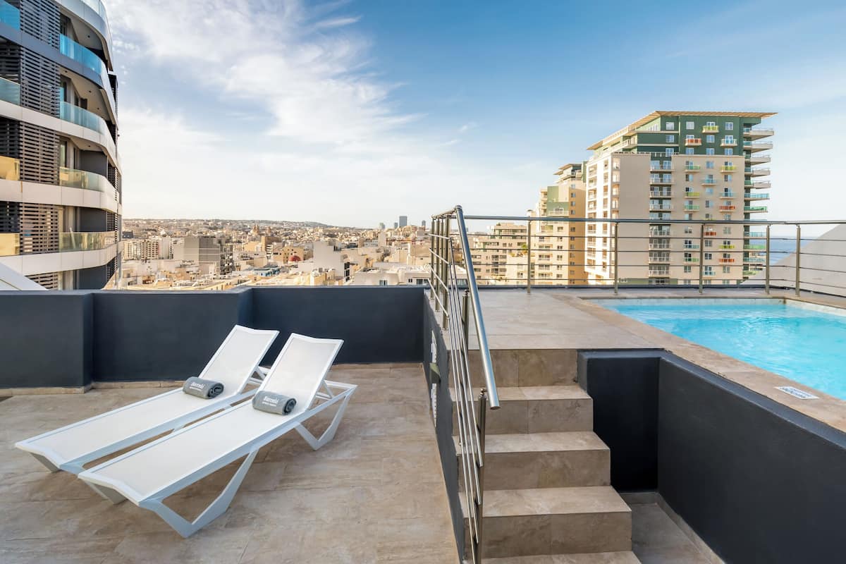 A rooftop pool area with lounge chairs and a view of the cityscape.