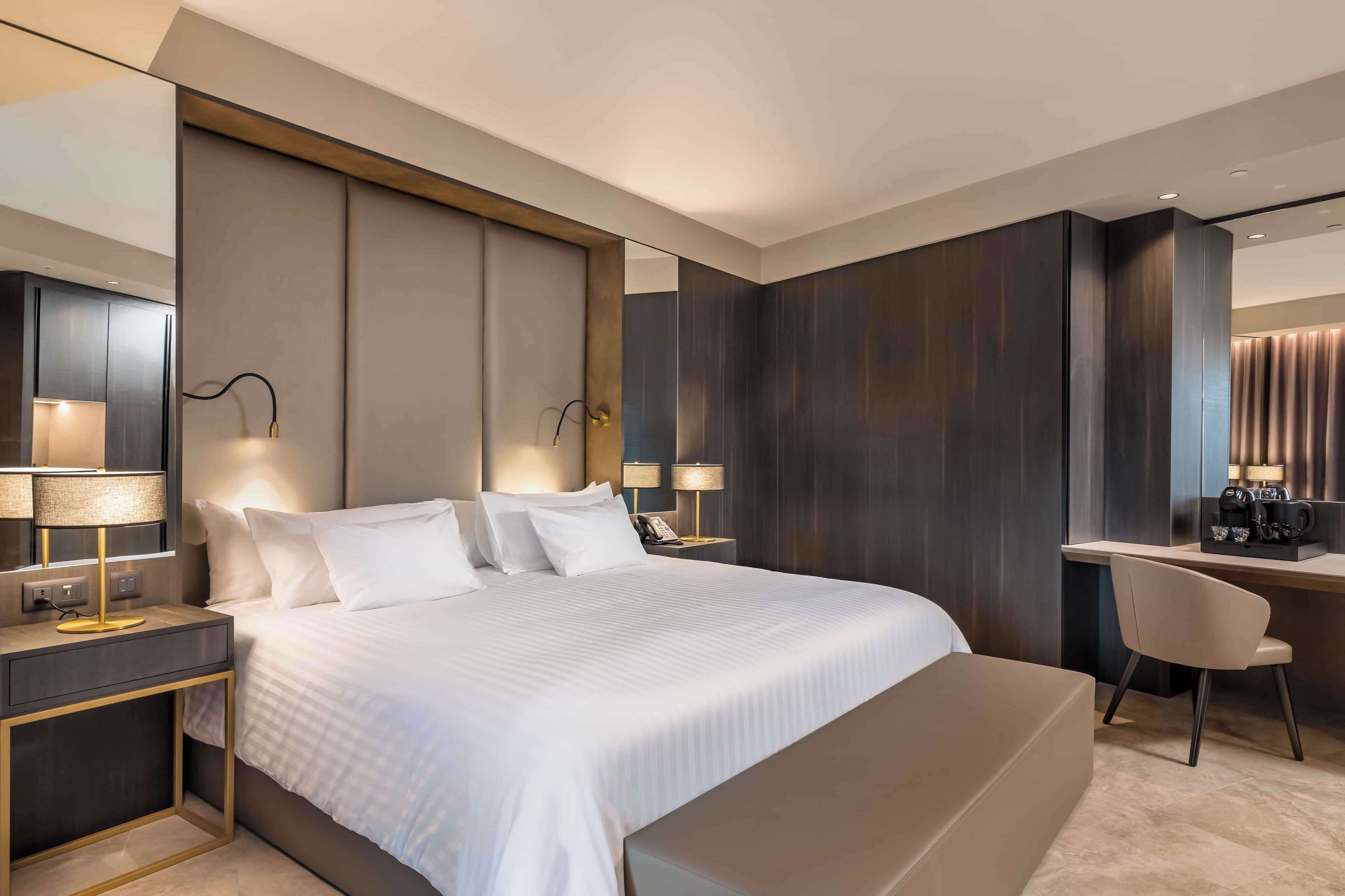 Una habitación de hotel moderna con una cama grande, lámparas de noche, un escritorio con silla y una cafetera.