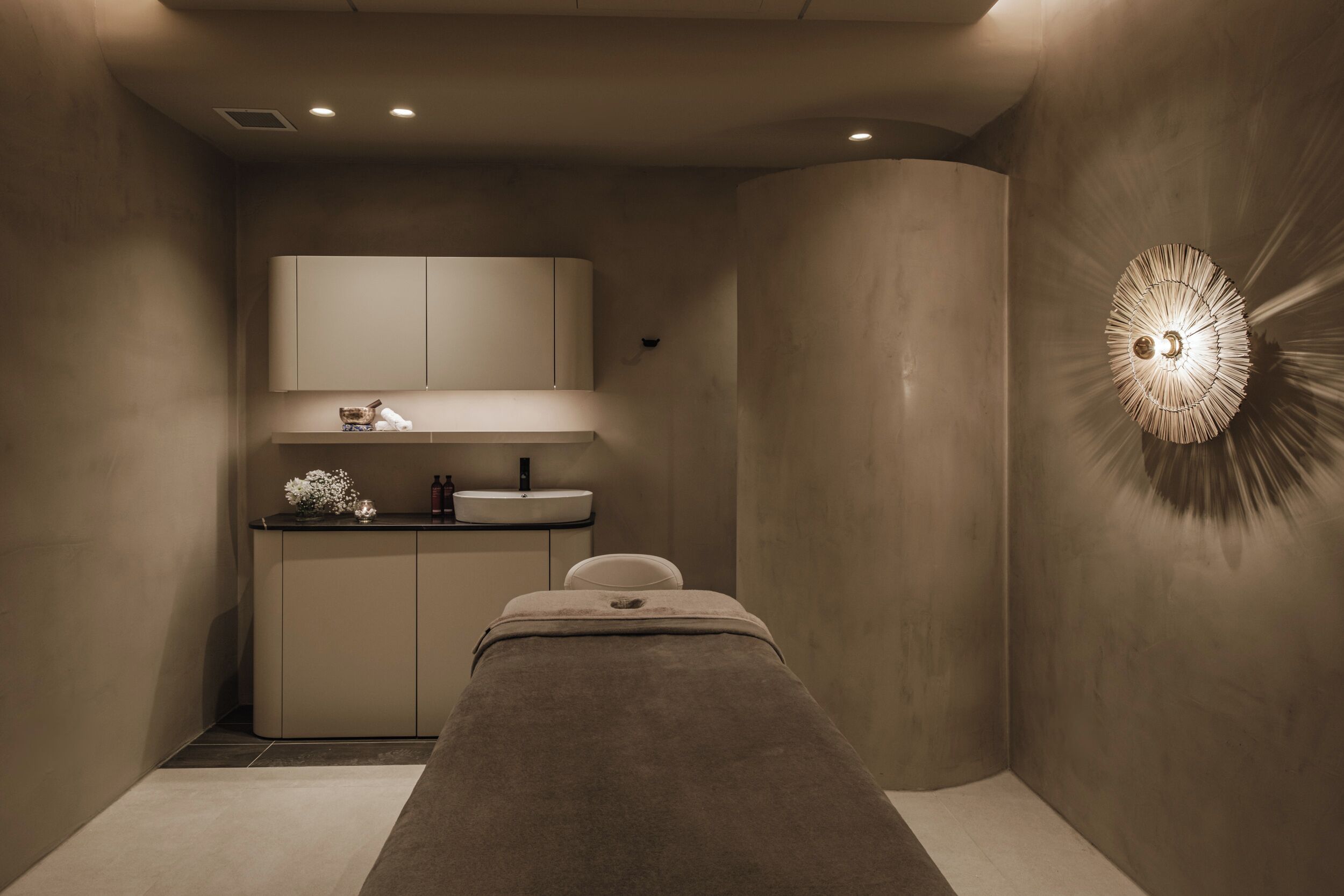 A spa room with a massage table, a sink, and a mirror above it.