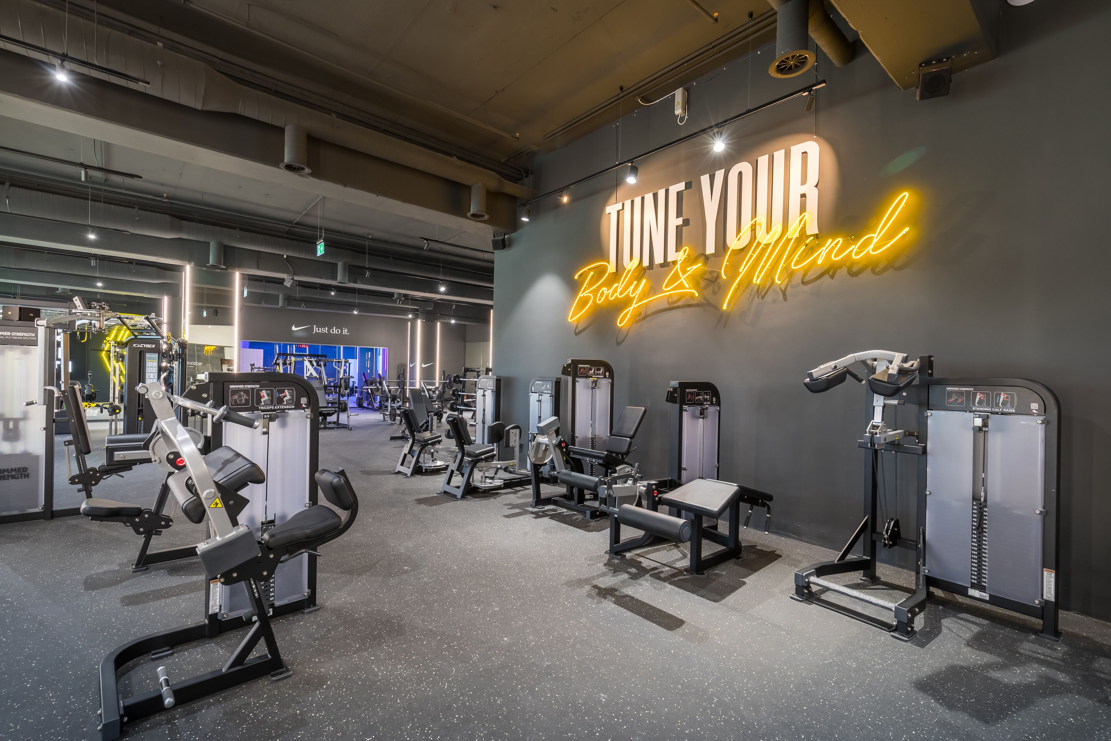 A gym with various exercise machines and a neon sign that reads "TUNE YOUR Body & Mind".